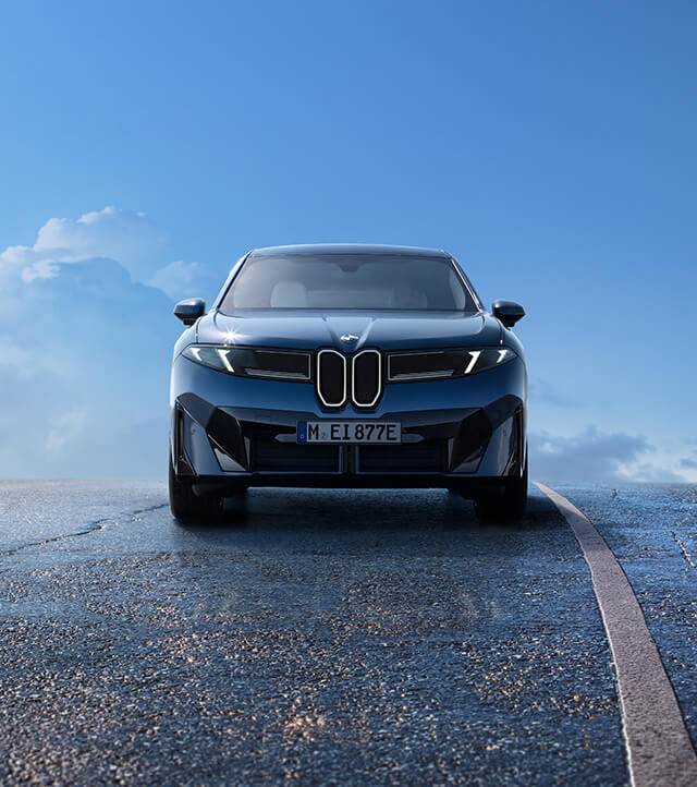 Autohaus-Praller-BMW-iX3-frontview Die neue Klasse BMW iX3 Elektroauto ist auf einer nassen Asphaltstraße unter einem blauen Himmel mit vereinzelten Wolken geparkt, gezeigt aus der Frontansicht. - AH Praller