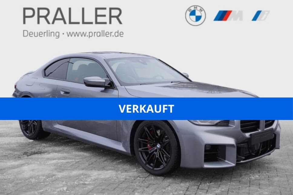Ein silbernes BMW Coupé parkt auf einer gepflasterten Fläche mit dem blauen Schriftzug VERKAUFT quer über dem Bild. Im Hintergrund weisen die Logos von BMW und PRALLER Deuerling www.praller.de auf exklusive BMW M Angebote der Autohaus Praller GmbH hin. - AH Praller